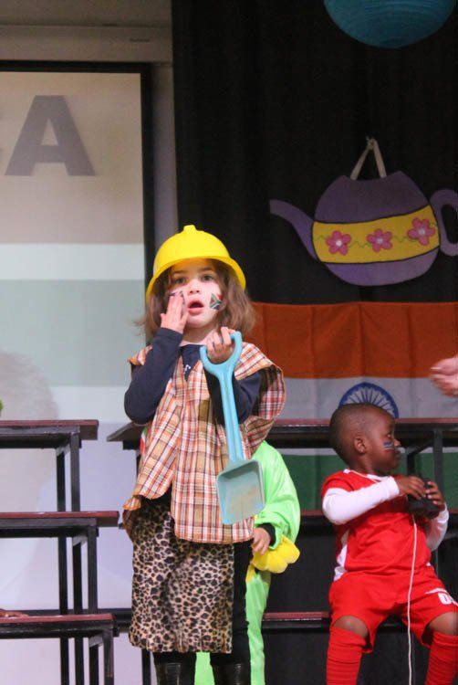 A little girl wearing a yellow hard hat holds a shovel
