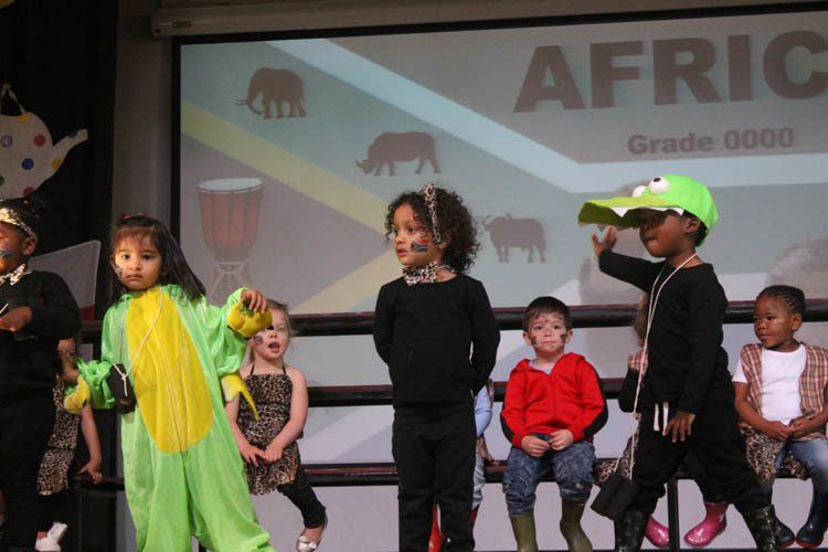 A group of children are standing on a stage in front of a screen that says africa