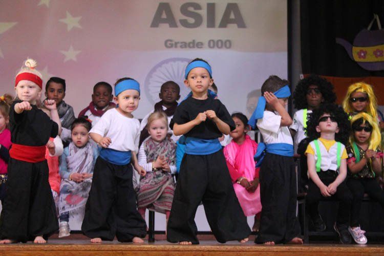 A group of children are dancing in front of a sign that says asia grade 000