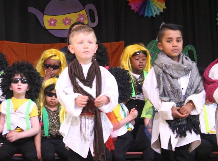 A group of children dressed in costumes are standing in front of a teapot