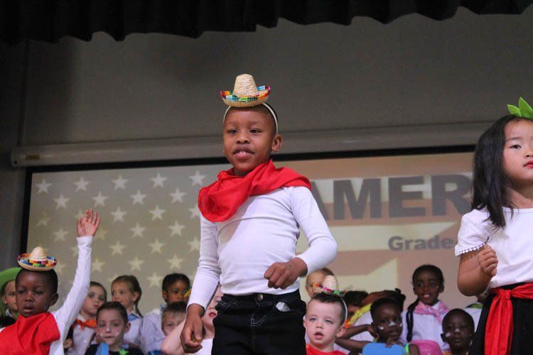A group of children are dancing on a stage in front of an american flag.