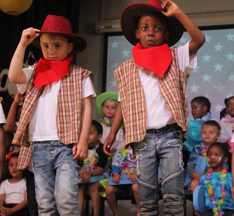 Two young boys dressed as cowboys are standing in front of a crowd