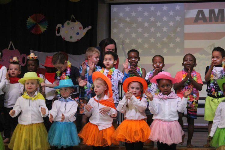 A group of children are dancing in front of an american flag.