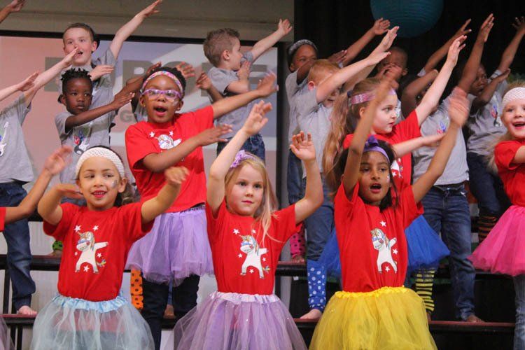 A group of children are standing on a stage with their arms in the air.