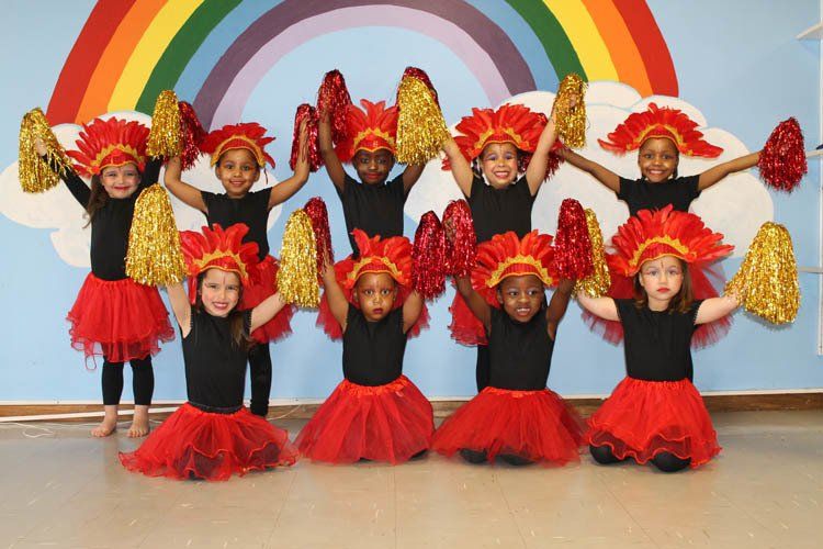 A group of young girls wearing red tutus holding pom poms in front of a rainbow