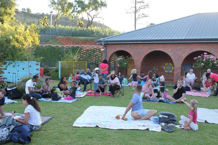 A group of people are sitting on blankets in the grass in front of a building.