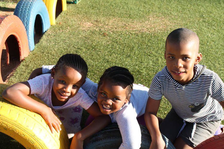 Three children are posing for a picture while sitting on a tire