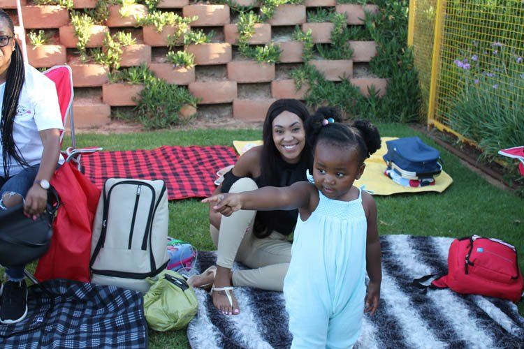A woman and a little girl are sitting on a blanket in the grass.