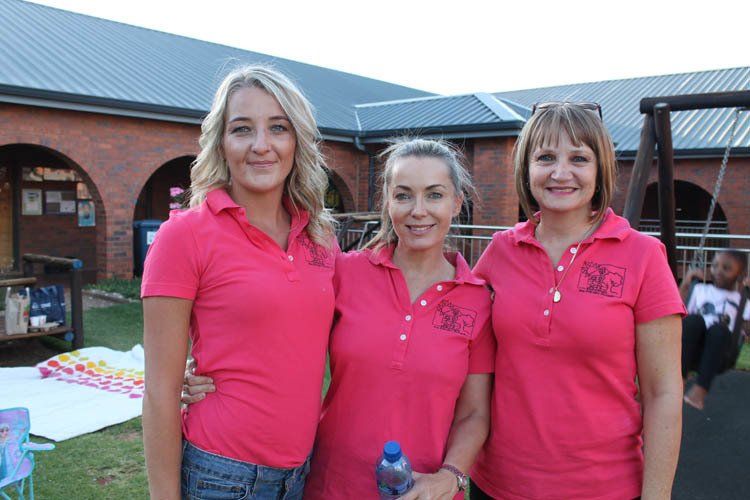 Three women wearing pink polo shirts are posing for a picture.