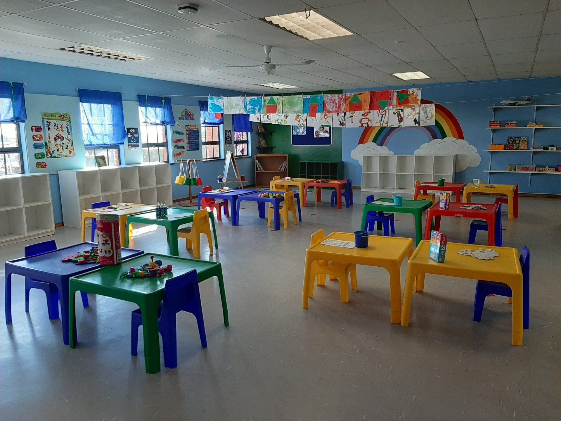 a classroom with tables and chairs and a rainbow on the wall