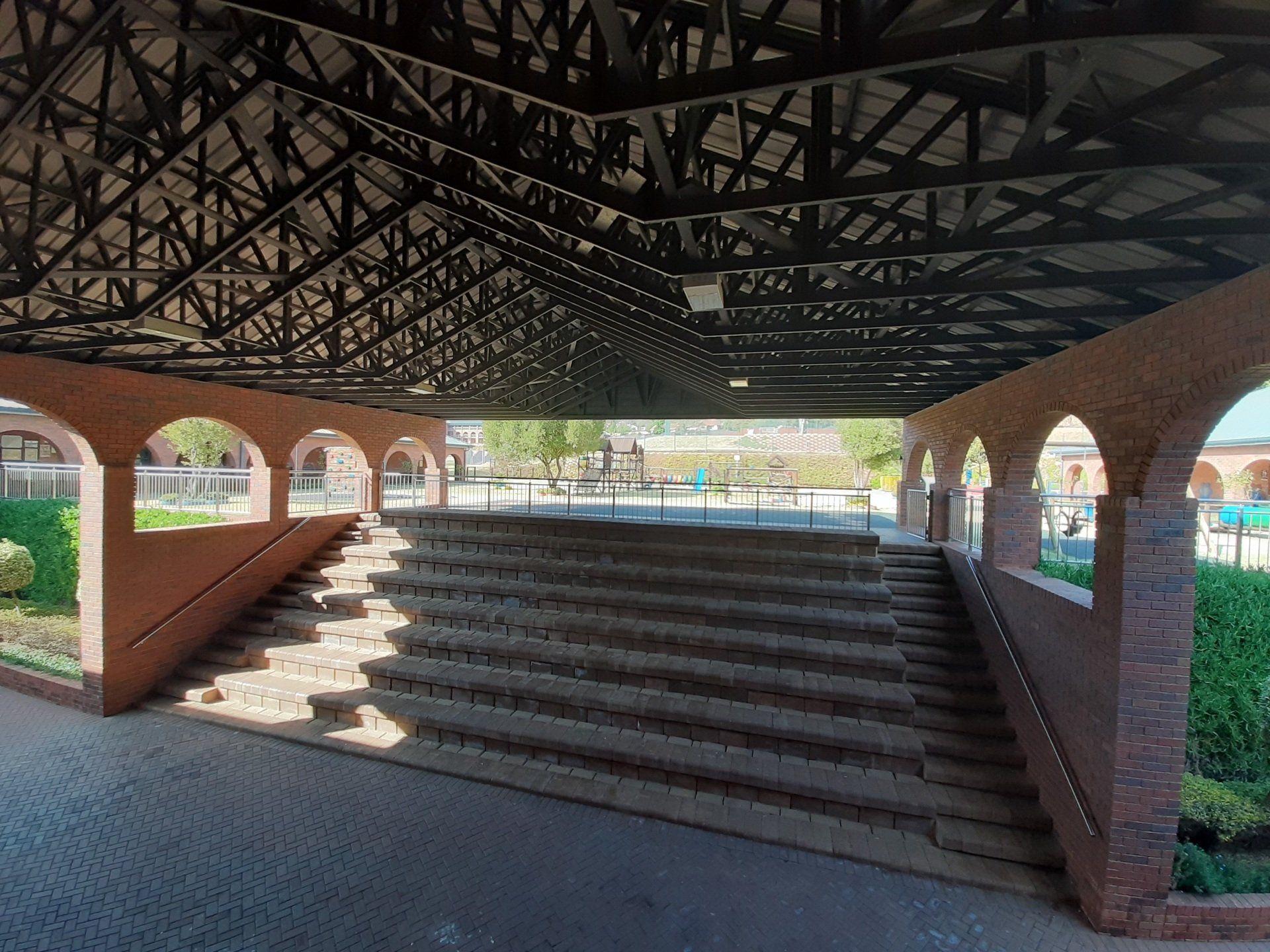 a brick amphitheater building with stairs leading up to it under a roof .