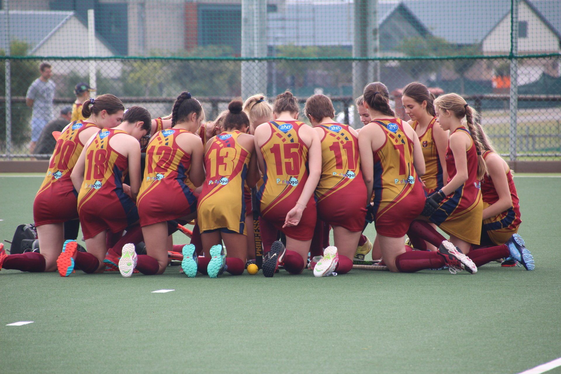 A group of female field hockey players are kneeling in a huddle on the field.