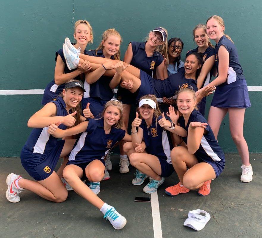 A group of young women are posing for a picture on a tennis court.