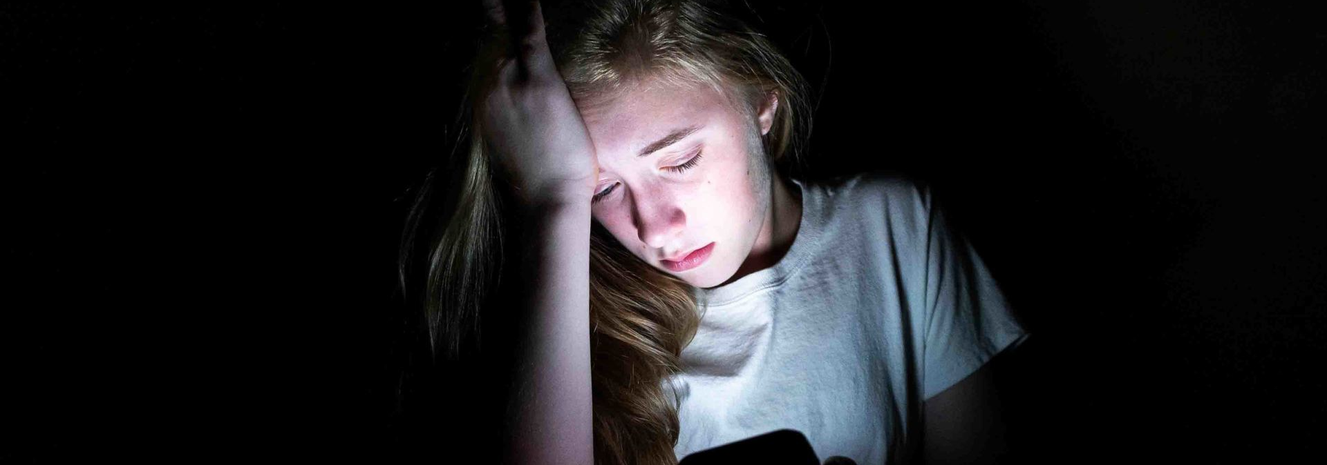 a sad girl in the dark looking at her phone
