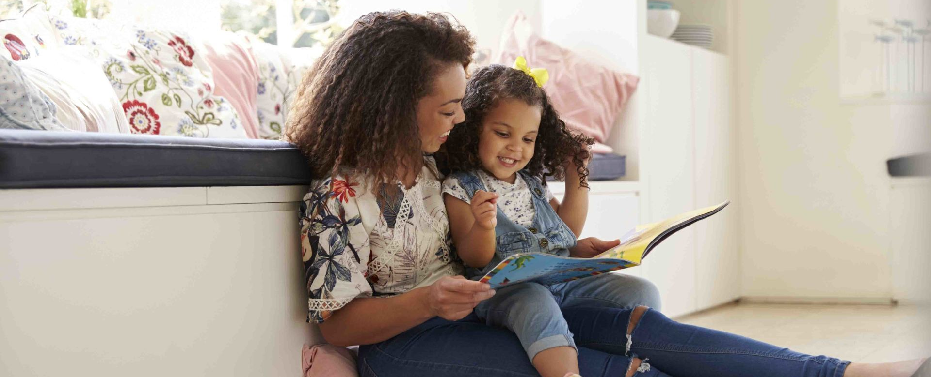 A woman and a little girl are sitting on a bench reading a book.