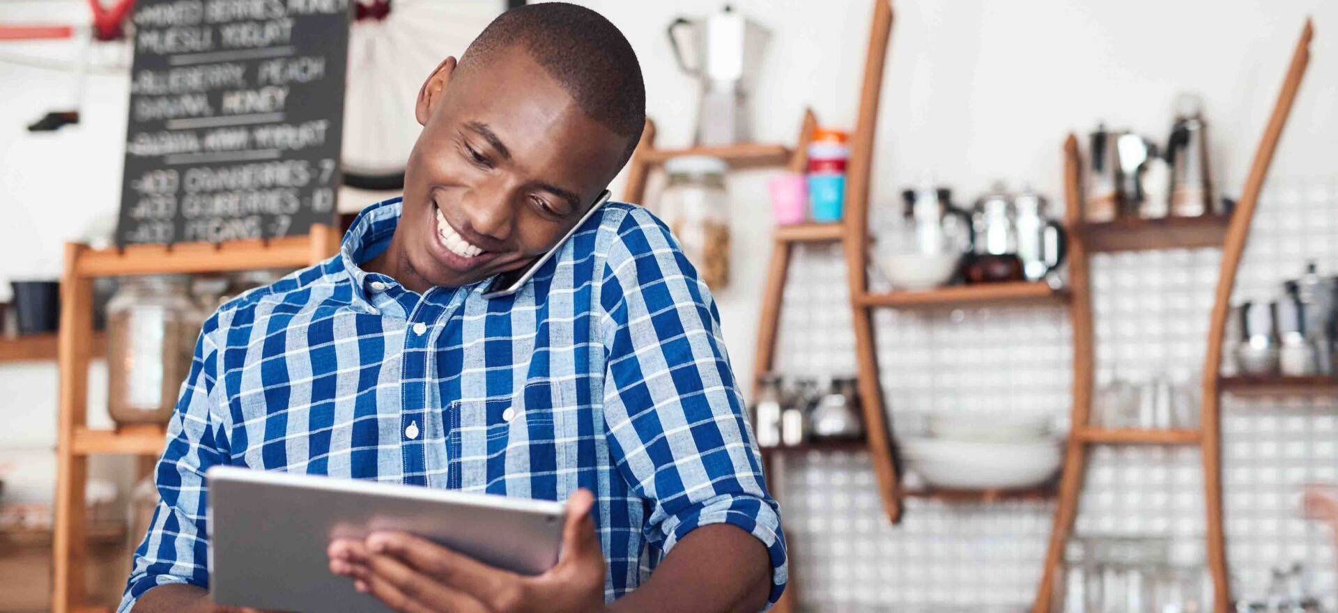 A man in a plaid shirt is smiling while using a tablet computer.