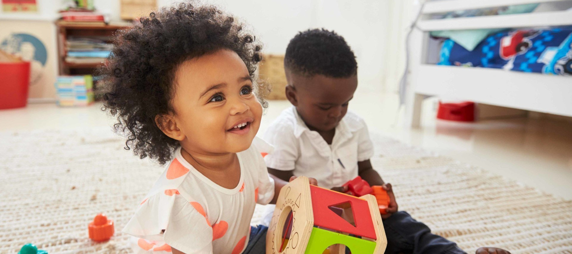 Two babies are sitting on the floor playing with toys.