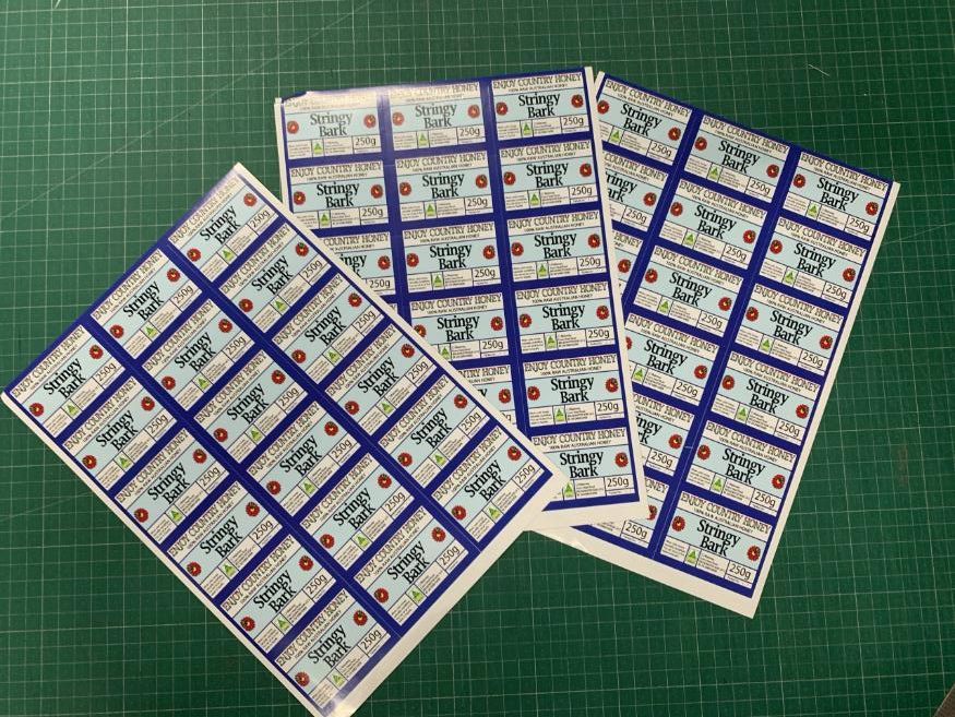 Three sheets of stickers are stacked on top of each other on a green cutting board — Copy That @ Profsec in Ballina, NSW