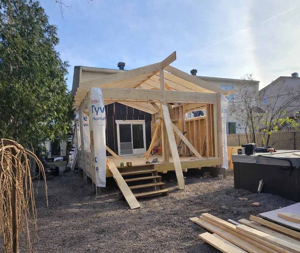 Partially built wooden porch frame with steps and a tarp-covered roof in a backyard yard
