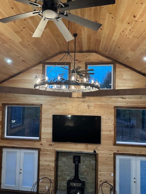 Wooden-paneled interior with windows, fireplace, TV, and a chandelier; ceiling fan and cabinets.