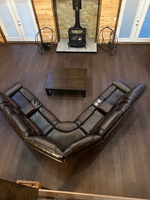 Dark leather sectional sofa in front of a fireplace, with a dark wood coffee table and hardwood floors.