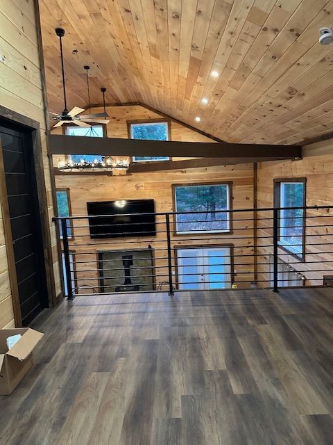 Interior of a cabin with wood walls, ceiling, and dark flooring. A black TV is mounted above a fireplace.