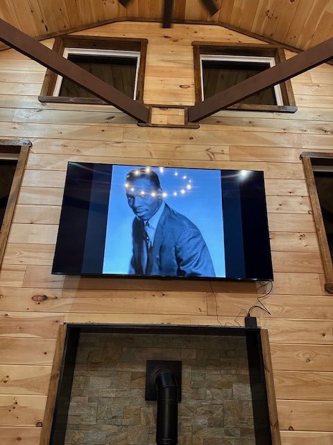 Black and white photo on TV: man in suit with a halo of lights against a blue background, wood paneled wall.