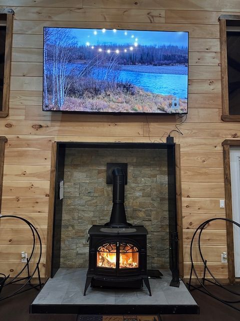 Living room with wood-burning stove beneath a large TV, set in a wood-paneled wall.