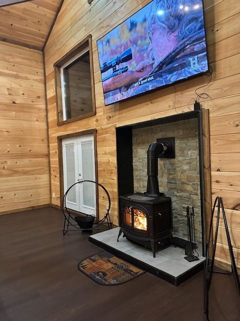 Cozy cabin interior with wood stove, TV above, and wood paneled walls.