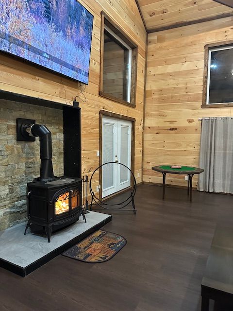 Cozy cabin interior with wood panel walls, fireplace, windows, and dark wood floor.
