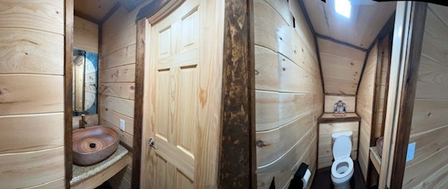 Small rustic bathroom with wooden walls, sink, toilet, and door.