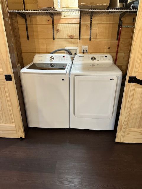White washer and dryer set in a wood-paneled laundry closet with shelves above.