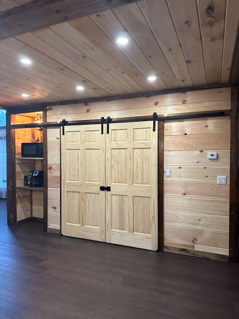 Wooden paneled room with light-colored barn doors on a black track. Built-in shelves and dark flooring are present.