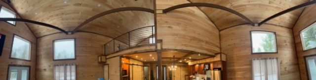 Wooden-walled room with curved ceiling and windows. A mezzanine level overlooks a lower area.