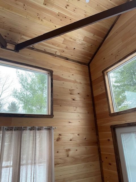 Interior of a room with wooden walls and ceiling, two windows, and a dark brown beam.