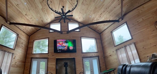 Wooden interior with a vaulted ceiling, TV, windows, and chandelier.