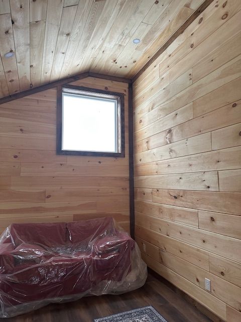 Interior of a room with wood paneling on the walls and ceiling, a window, and a red couch covered in plastic.