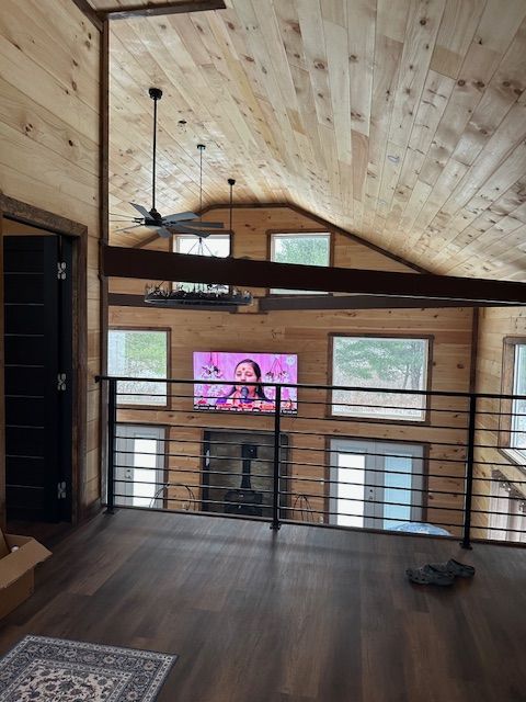 Interior loft space with wooden walls and ceiling, a TV above a fireplace, and black railing.
