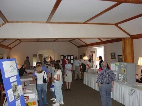 People browse displays at an event in a bright room with exposed beams.