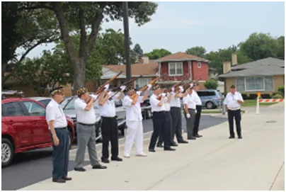 Men in uniforms firing rifles outside houses; ceremonial salute.