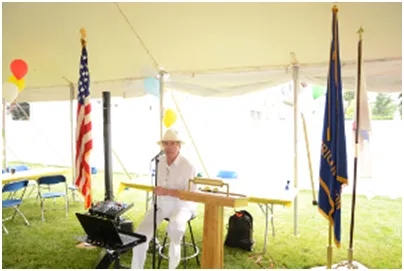 Man in white at a podium under a tent, with US and other flags.