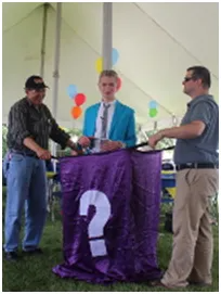 Three men performing a magic trick outdoors with a purple box and question mark.