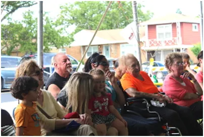 People of diverse ages and ethnicities gathered under a tent, watching something outdoors.