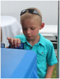 Boy in teal shirt plays with something blue. Sunglasses atop his head.