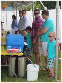 People at an outdoor party: adults, children, food and drinks, under a tent.