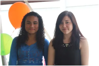 Two young women smiling in front of a bright window.