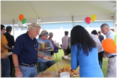 People at an outdoor event with food; balloons overhead.