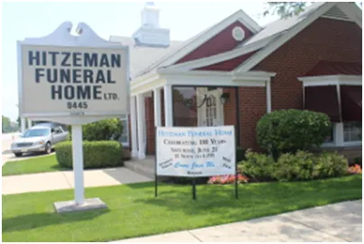 Hitzeman Funeral Home building with sign. Red brick and white trim. Sign reads