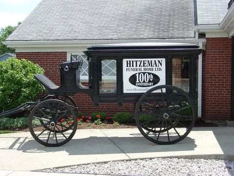 Black hearse on display in front of the Hitzeman Funeral Home, with brick building in background.