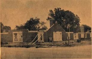 Brick structure under construction, with windows and chimney. Construction materials and trees surround the building.